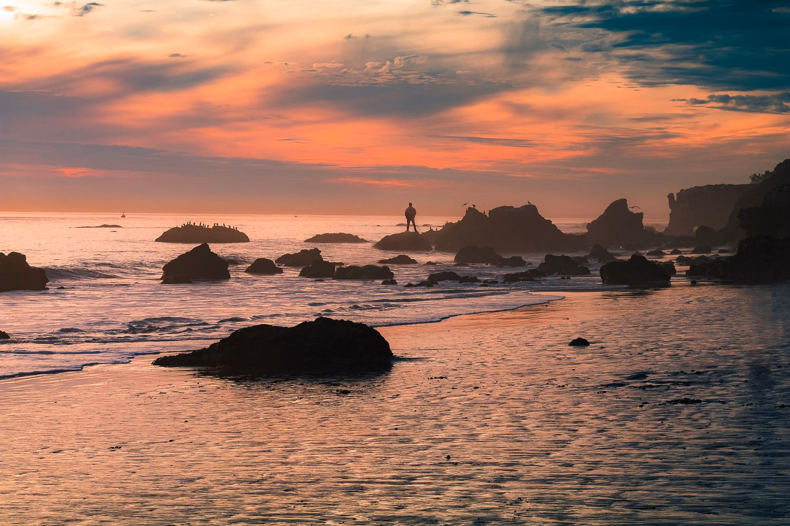 Pastel sunset over rocks and wet sand on a Southern California beach